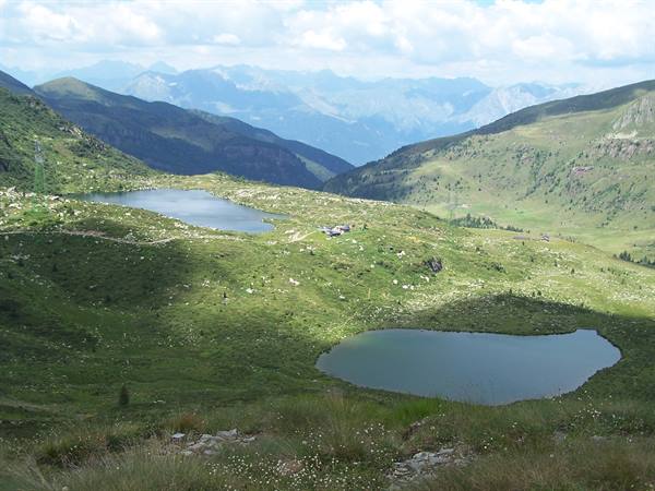 Two alpine lakes among green pastures and mountains under white clouds