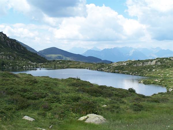 Alpine lake surrounded by green grass and rocks, blue mountains behind