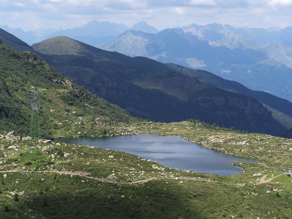 Alpine lake among green meadows and rocks, power pylon, blue mountains