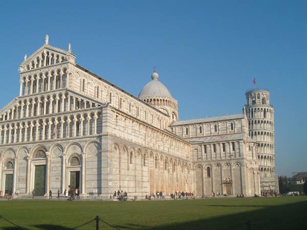 Pisa Cathedral in white marble with the Leaning Tower, blue sky and green lawn