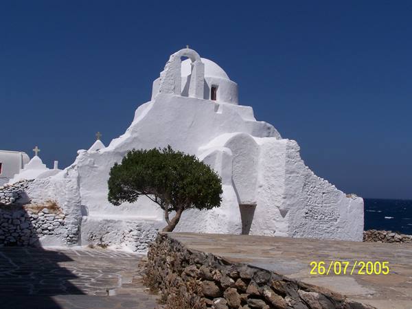 White Paraportiani church in Mykonos, tree in front, blue sky
