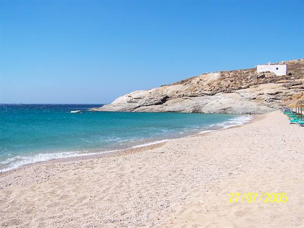 Pale sandy beach, smooth rock, white house, umbrellas and turquoise sea
