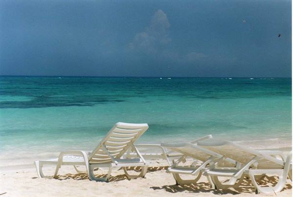 Empty white lounge chairs on the sand before a turquoise sea