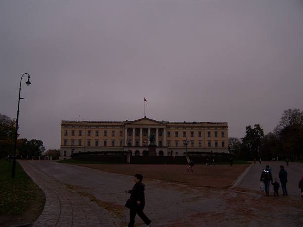 Royal Palace in Oslo with red flag, grey dusk sky, pedestrians walking