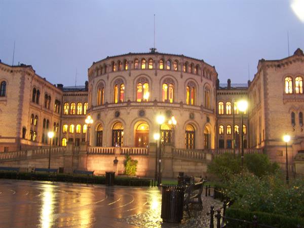 Oslo's Stortinget parliament lit at dusk, rain-soaked square reflecting lights