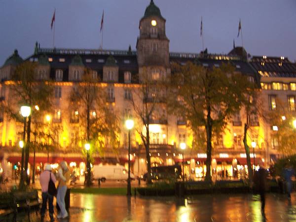 Illuminated building with clock tower in Oslo, rain and blurred pedestrians