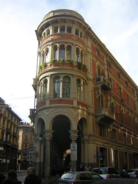 Red-brick palace with octagonal tower and arcades at a Bologna street corner