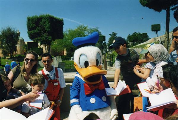 Donald Duck signing autographs for tourists at Disneyland, sunny day with trees