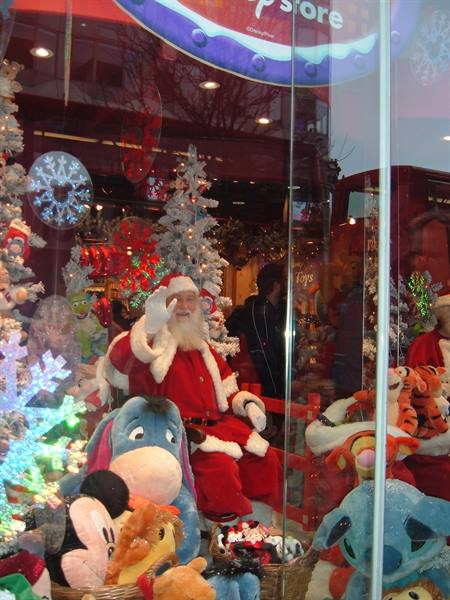 Santa Claus waves among snowy trees and Disney plush toys in shop window