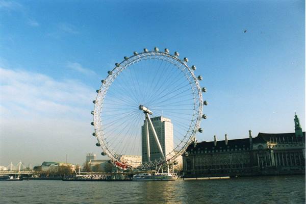 The London Eye by the misty Thames, with a tower and historic building behind