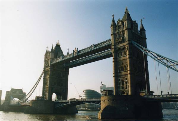 Stone tower of Tower Bridge against blue sky, pedestrians cross the Thames bridge