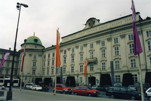 Imperial palace with green dome in Innsbruck, colorful flags, cars under gray sky