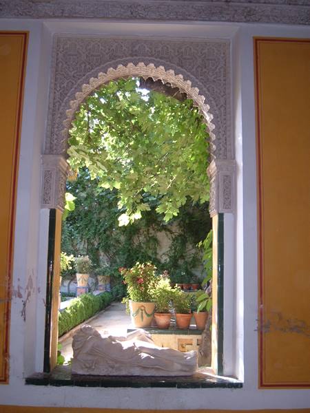 Carved stucco arch framing a green courtyard with terracotta pots and ochre walls