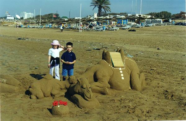 Children beside sand sculptures shaped like camels on the beach