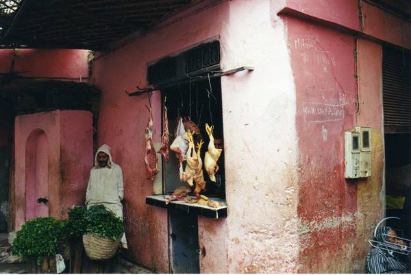 Butcher outside his pink shop with hanging meat and chickens in Marrakech medina