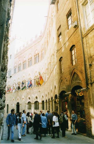 Tourists on the square beneath Siena's Palazzo Pubblico with flags