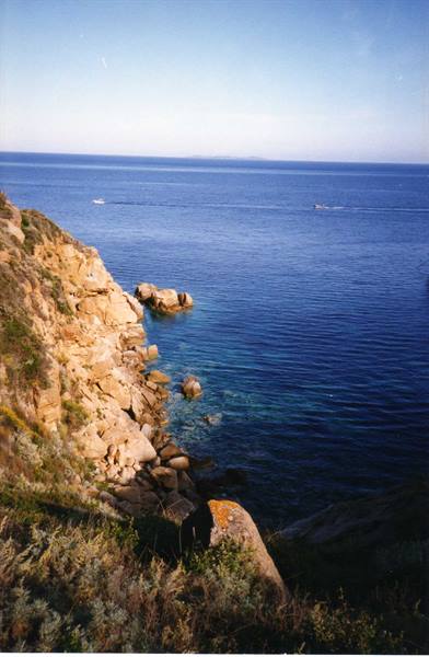 granite rocks with Mediterranean shrubs above blue sea and boats