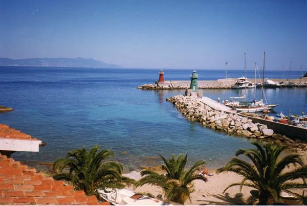 Small harbour with rocky breakwater, two lighthouses, sailboats and palms on beach