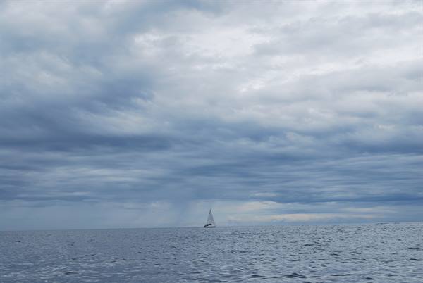 Lone sailboat on gray sea under heavy storm clouds