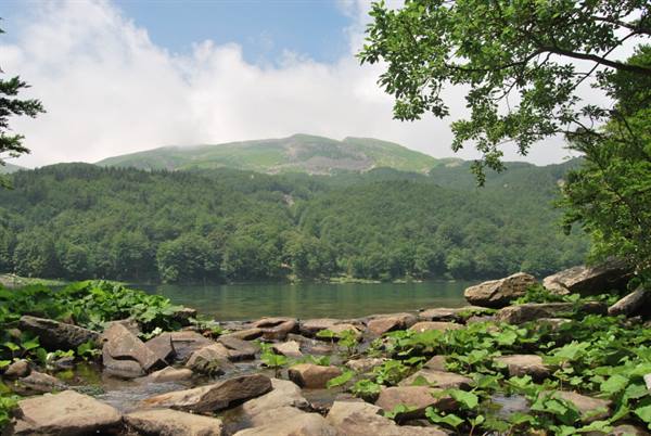 Granite boulders on mountain lake, forested slopes under clouds