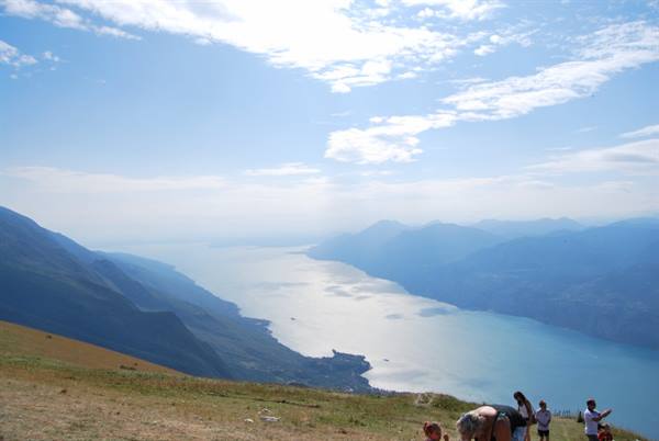 Tourists on Monte Baldo meadow overlooking Lake Garda surrounded by mountains