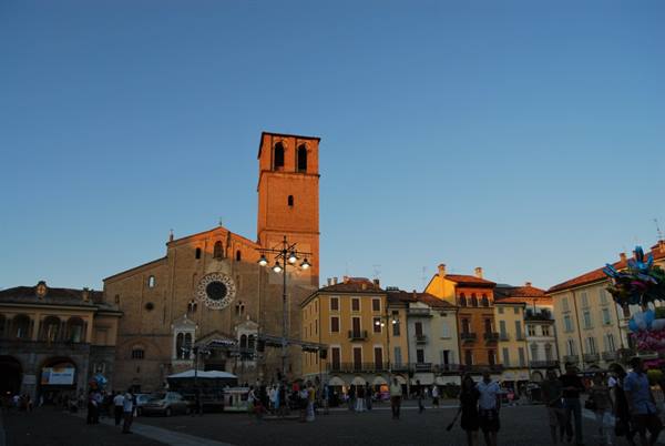 Square with Romanesque basilica and brick tower, people strolling in golden evening light