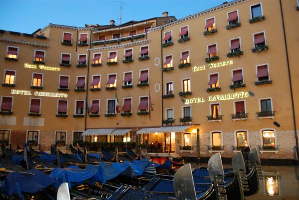 Hotel Cavalletto in Venice, lit yellow facade, blue-covered gondolas moored in front
