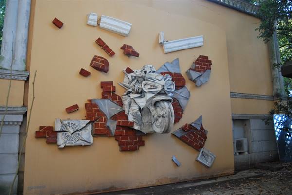 Stone motorcycle sculpture bursting through ochre wall with bricks, natural daylight