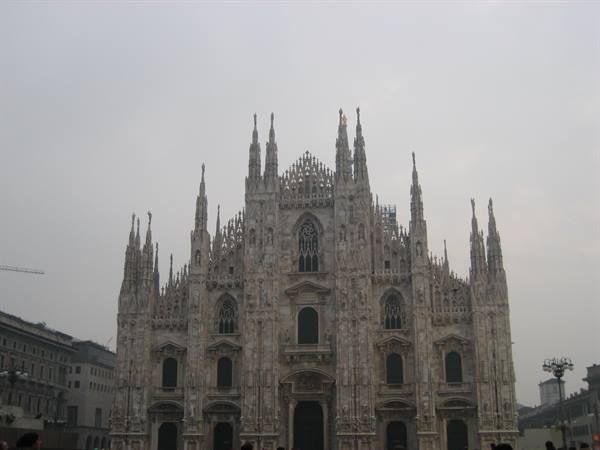 Milan Cathedral, white marble facade among gothic spires, grey sky