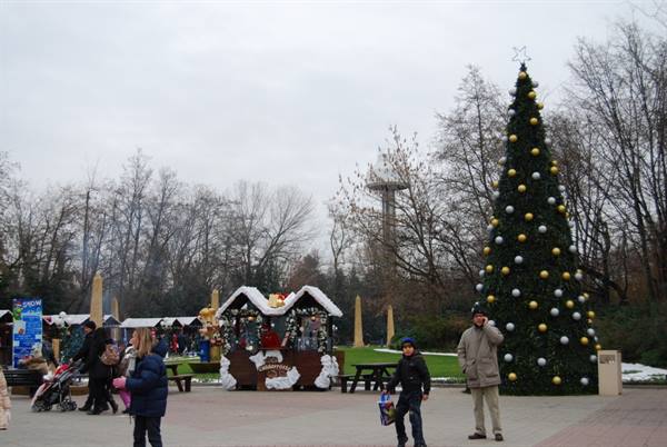 Decorated Christmas tree beside wooden chalets in snowy park with strollers