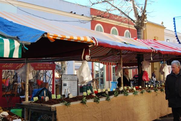 Open-air market stall with striped awnings, olives and spices displayed, man strolling past