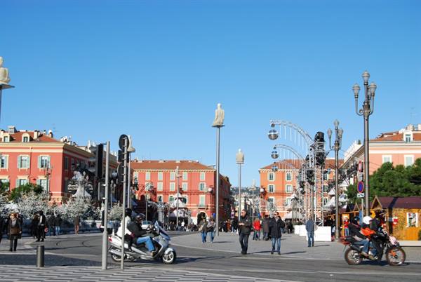 Place Masséna in Nice: pedestrians and scooters cross the square among statues and Christmas lights