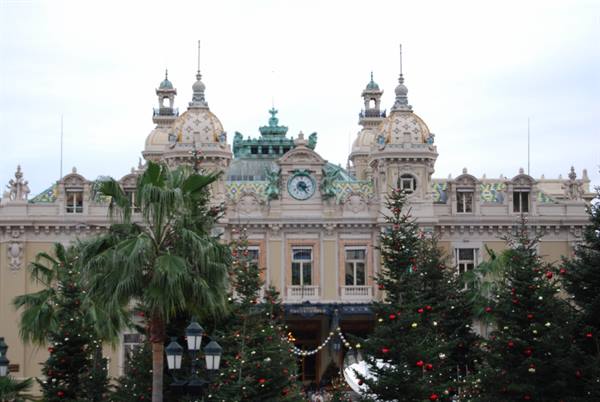 Monte Carlo Casino facade framed by Christmas trees and palms, grey sky