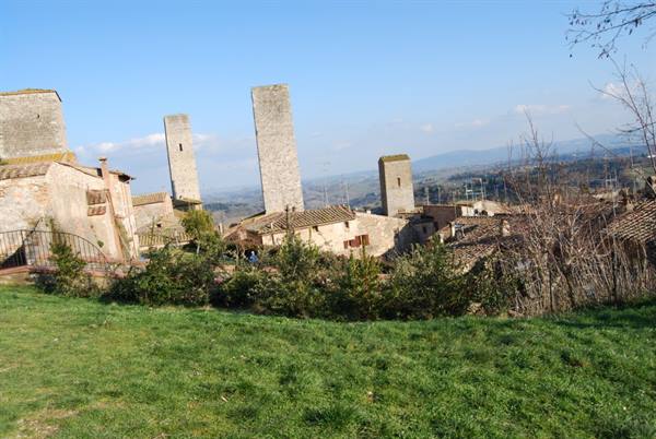 Medieval towers of San Gimignano above rooftops, green lawn and blue sky