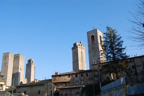 Medieval stone towers of San Gimignano rising above rooftops, blue sky