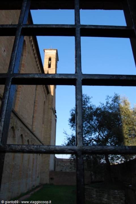 Medieval brick bell tower seen through black iron bars, trees under blue sky
