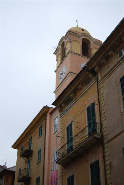 Yellow bell tower with clock and dome above ochre houses with iron balconies