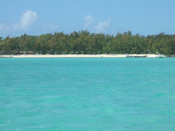 Turquoise water in front of white beach with umbrellas and boat