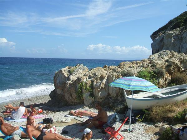Sunbathers on pebble beach, striped umbrella and rowboat beside the rocks