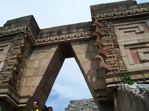 Stone doorway with carved geometric fretwork and Tlaloc masks, visitors below