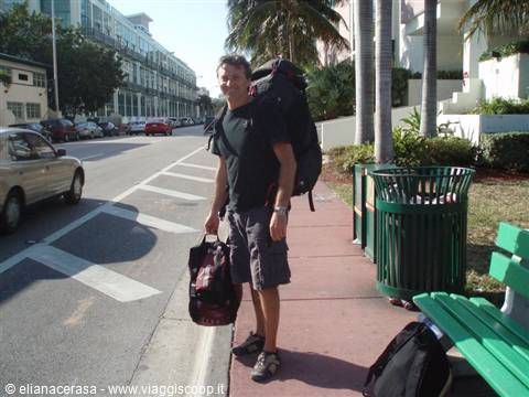 Traveler with big backpack and duffel bag on a sidewalk lined with palms