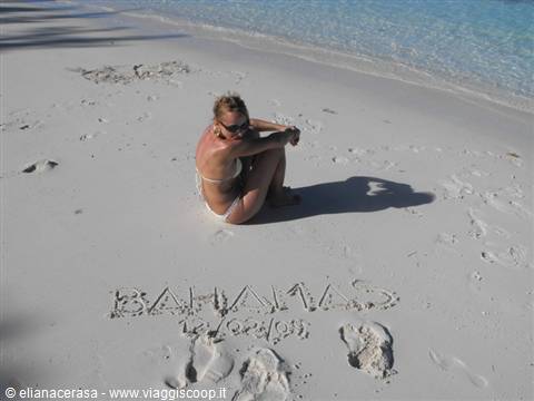 Woman in bikini sitting on white sand with Bahamas written on it