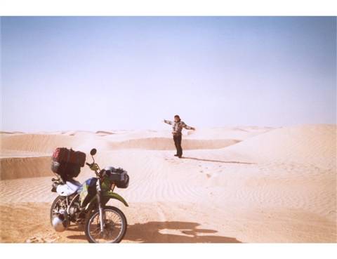 Motorcycle loaded with luggage on sand dunes, man standing among the dunes