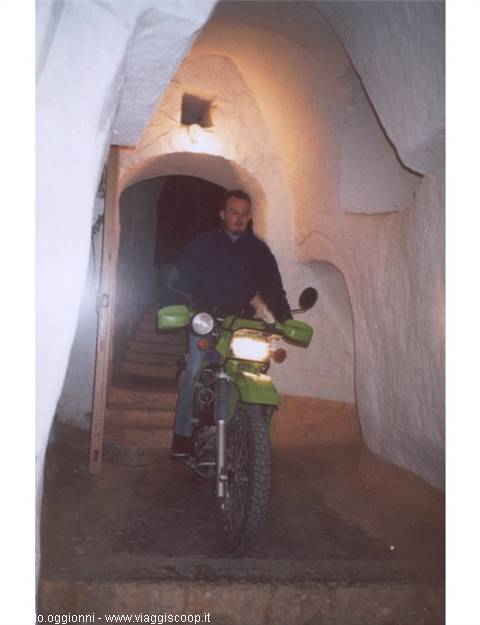 Man on green motorbike inside a whitewashed arched alleyway