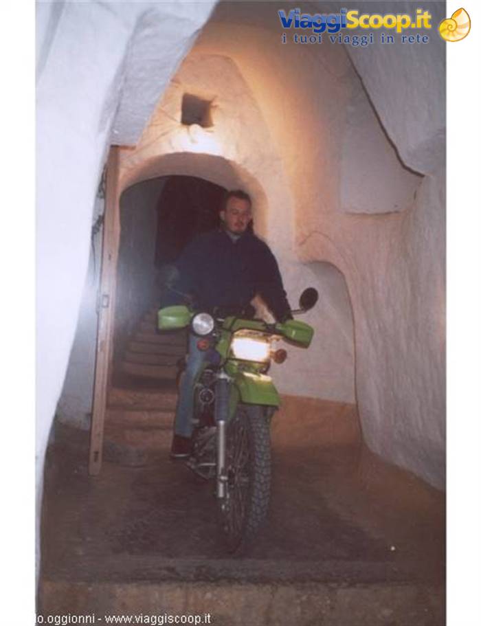 Man on green motorbike inside a whitewashed arched alleyway