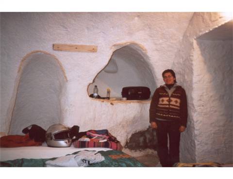 Woman in sweater inside a whitewashed cave room, motorcycle helmet on bed