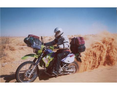 Helmeted rider with luggage raises sand while riding through the desert