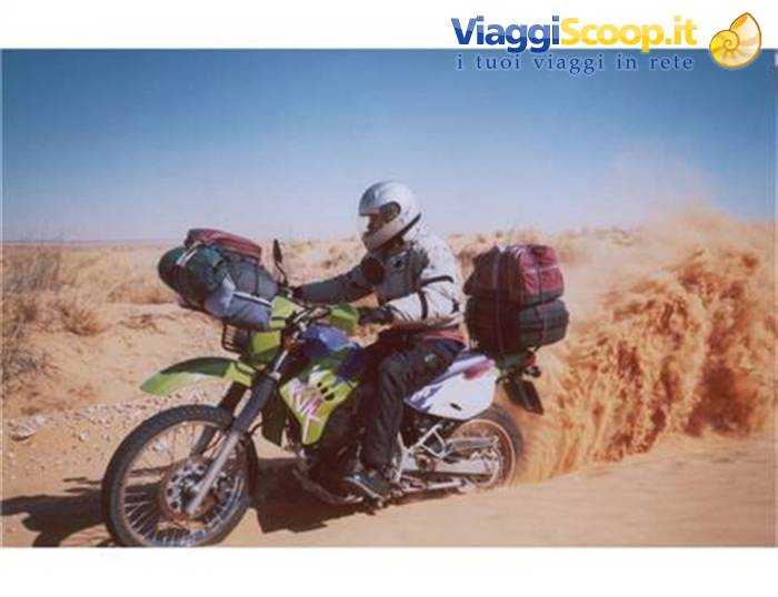 Helmeted rider with luggage raises sand while riding through the desert