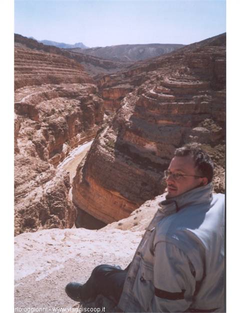 Man sitting on rock in front of a sandstone canyon with dry riverbed
