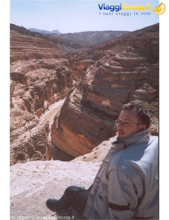 Man sitting on rock in front of a sandstone canyon with dry riverbed